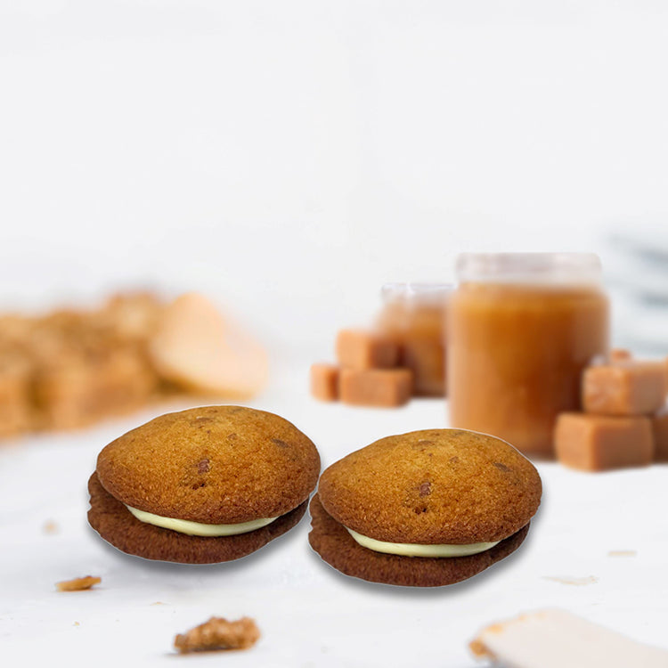Two cookie sandwiches with cream filling on a white surface with blurred background